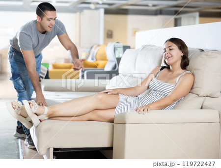 Couple chooses furniture in store.Wife is sitting on sofa,husband is standing next to her 119722427
