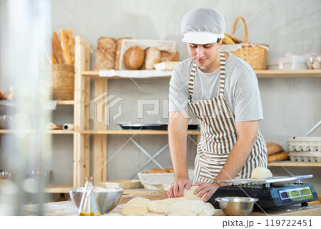 Male baker stands at his work bench, kneading and shaping dough to make bread, croissants and baguettes Male baker stands at his work bench, kneading and shaping dough to make bread, croissants and baguettes 119722451