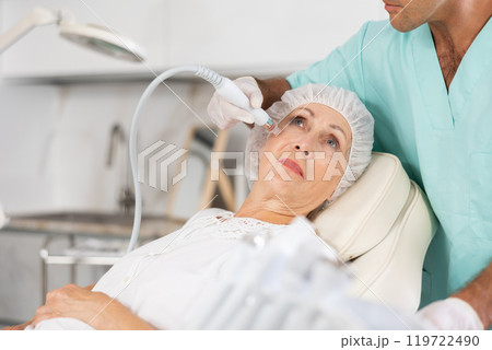 Male dermatologist performing cosmetology procedure for elderly woman, RF lifting and deep hydration for facial skin therapy Male dermatologist performing cosmetology procedure for elderly woman, RF lifting and deep hydration for facial skin therapy 119722490