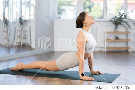 Sportive woman performing cobra pose of yoga during training in training room Sportive woman performing cobra pose of yoga during training in training room 119722559