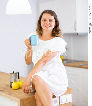 Young woman sitting on kitchen table with cup 119722742