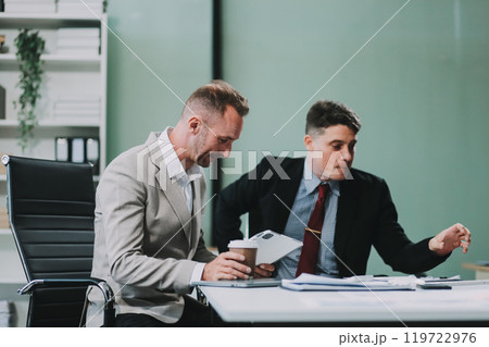 Two happy colleagues with laptop and documents in office Two happy colleagues with laptop and documents in office 119722976