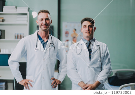 Portrait of two dedicated doctors smiling and looking at camera while holding a tablet and a diary in clinic. Two smiling doctors in white coat working in an office and looking at camera. 119723002