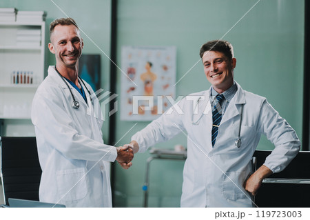Portrait of two dedicated doctors smiling and looking at camera while holding a tablet and a diary in clinic. Two smiling doctors in white coat working in an office and looking at camera. 119723003
