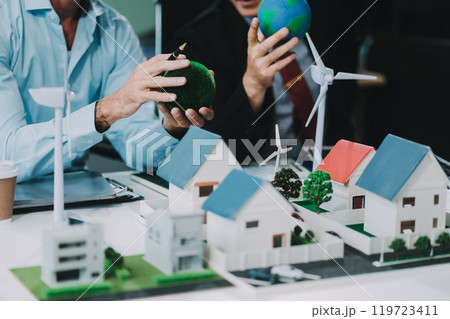 Engineers meeting about wind turbine model and house model. Renewable energy and housing development concept. Team of architects and engineers in modern office discussing design structure. Engineers meeting about wind turbine model and house model. Renewable energy and housing development concept. Team of architects and engineers in modern office discussing design structure. 119723411