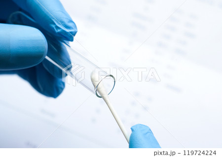 Doctor holds a COVID-19 swab collection, wears blue gloves and a PPE protective mask, and carries a test tube to collect the OP NP and  test coronavirus. 119724224