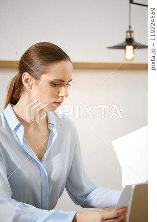 Focused woman working diligently on a document in a stylish office during the daytime Focused woman working diligently on a document in a stylish office during the daytime 119724589
