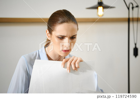 Concerned woman reviewing important documents in a bright office setting in the morning Concerned woman reviewing important documents in a bright office setting in the morning 119724590