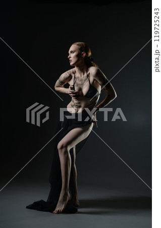 Artistic expression through dance and pose by a model in a dark studio setting 119725243