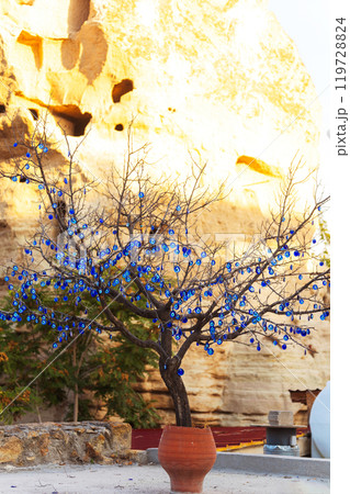 There is a beautiful tree placed in a pot adorned with blue glasses devil eyes.  119728824