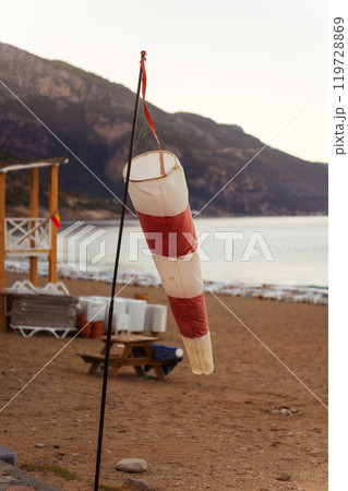 A colorful red and white wind vane is hanging from a tall pole on the beach A colorful red and white wind vane is hanging from a tall pole on the beach 119728869