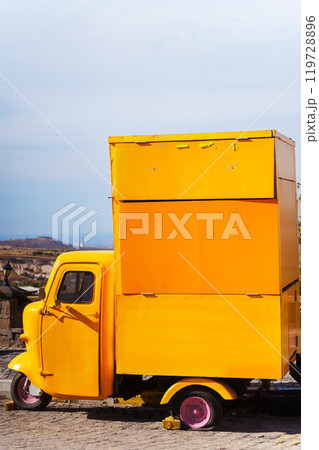 A yellow truck is parked by the road in front of a mountain 119728896