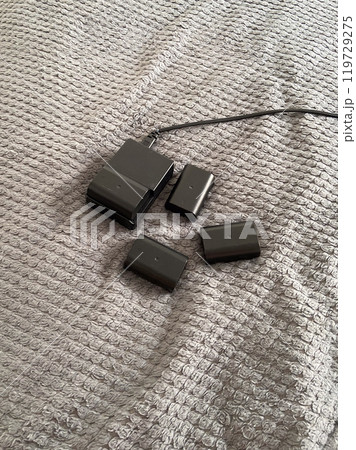 Set of camera batteries and a charger lie neatly arranged on a textured gray surface, ready for use. This image portrays a sense of preparation and practicality in the world of photography Set of camera batteries and a charger lie neatly arranged on a textured gray surface, ready for use. This image portrays a sense of preparation and practicality in the world of photography 119729275