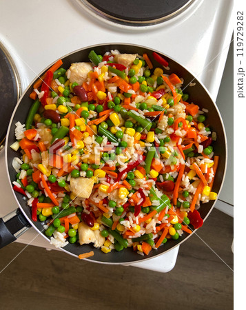 Vibrant stir-fry of colorful vegetables and rice in a pan creates a lively and delicious visual feast. The dish's bright hues and variety of ingredients highlight the joy and creativity of cooking at 119729282