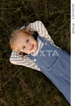 A young girl is laying on the grass, smiling and looking up at the camera A young girl is laying on the grass, smiling and looking up at the camera 119729293