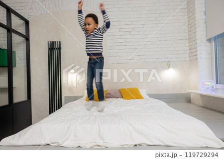 Kid jumping on the bed and looking enjoyed and contented Kid jumping on the bed and looking enjoyed and contented 119729294