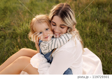 A woman is holding a baby girl in a grassy field 119729301