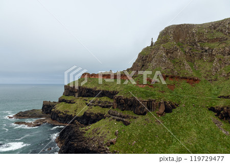 Coastal cliffs at Giant Causeway black basalt red rock layers overlooking rough Atlantic Ocean 119729477