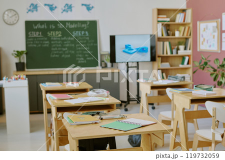 Well-organized classroom setup with study materials neatly arranged on tables and a chalkboard in background. Bookshelves filled with educational resources flank sides of room Well-organized classroom setup with study materials neatly arranged on tables and a chalkboard in background. Bookshelves filled with educational resources flank sides of room 119732059