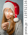 Sparkler in shape of star in hand beautiful girl with long red hair in Santa hat on grey background. 119732116