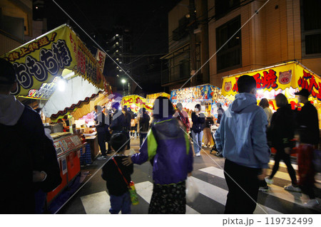 縁日の夜は露店の灯りが人々を呼び込む。暖かい光の中で金魚すくいや食べ歩き 119732499