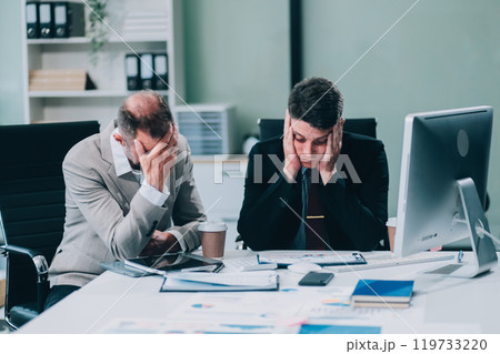 Two Unhappy tired businessman, corporate manager, sits at the workplace, tired from online work, stressed, nervous, massages the bridge of his nose, closed his eyes, experiencing a headache. Two Unhappy tired businessman, corporate manager, sits at the workplace, tired from online work, stressed, nervous, massages the bridge of his nose, closed his eyes, experiencing a headache. 119733220
