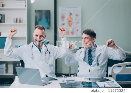 Smiling young male clinician shake hands with happy teammate appreciate for assistance on surgery show support respect on team council. Two doctors partners handshaking making deal reaching agreement Smiling young male clinician shake hands with happy teammate appreciate for assistance on surgery show support respect on team council. Two doctors partners handshaking making deal reaching agreement 119733244