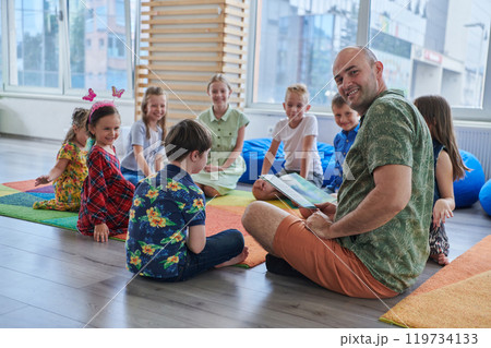 Reading time in an elementary school or kindergarten, a teacher reading a book to children in an elementary school or kindergarten. The concept of pre-school education. Selective focus Reading time in an elementary school or kindergarten, a teacher reading a book to children in an elementary school or kindergarten. The concept of pre-school education. Selective focus 119734133