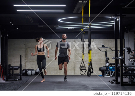 A fit couple in a modern gym, engaging in running exercises and showcasing their athletic prowess with a dynamic start. A fit couple in a modern gym, engaging in running exercises and showcasing their athletic prowess with a dynamic start. 119734136