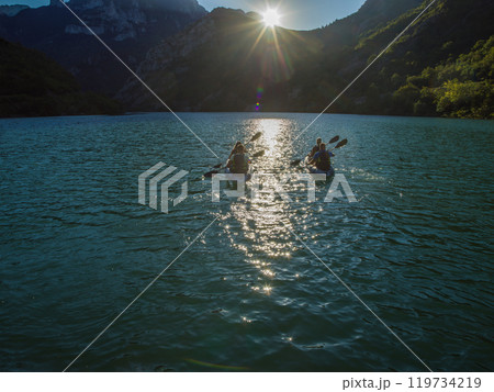 A group of friends enjoying fun and kayaking exploring the calm river, surrounding forest and large natural river canyons during an idyllic sunset. 119734219