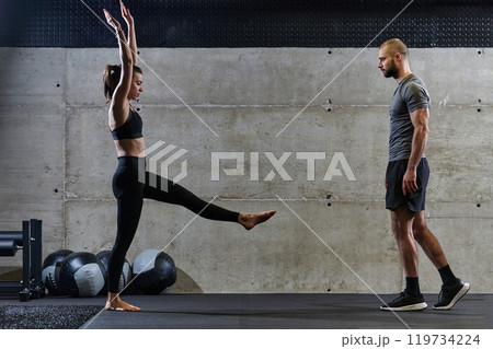 A muscular man assisting a fit woman in a modern gym as they engage in various body exercises and muscle stretches, showcasing their dedication to fitness and benefiting from teamwork and support A muscular man assisting a fit woman in a modern gym as they engage in various body exercises and muscle stretches, showcasing their dedication to fitness and benefiting from teamwork and support 119734224