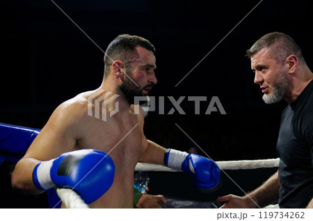 Cornered boxer receives strategic advice from trainer during intense bout. Cornered boxer receives strategic advice from trainer during intense bout. 119734262
