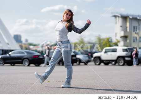 Young woman dancing in a parking lot on a sunny day with urban backdrop 119734636