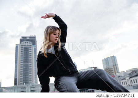 Young dancer performing a graceful movement on a rooftop in the city Young dancer performing a graceful movement on a rooftop in the city 119734711