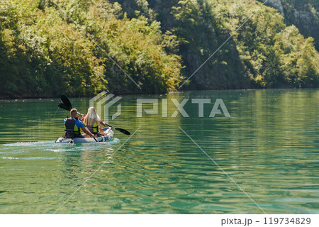A young couple enjoying an idyllic kayak ride in the middle of a beautiful river surrounded by forest greenery A young couple enjoying an idyllic kayak ride in the middle of a beautiful river surrounded by forest greenery 119734829
