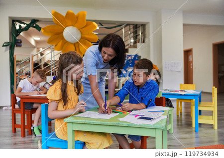 Creative kids during an art class in a daycare center or elementary school classroom drawing with female teacher. 119734934