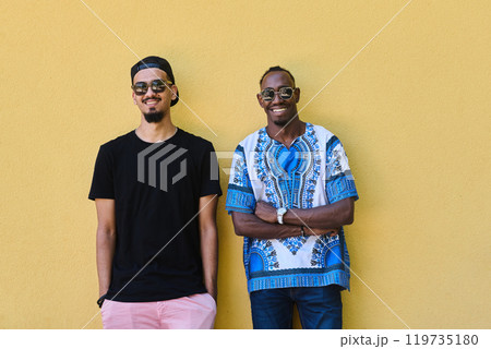 Two Male Friends: African American Teenager in Sudanese Traditional Attire Leaning Against Yellow Wall 119735180