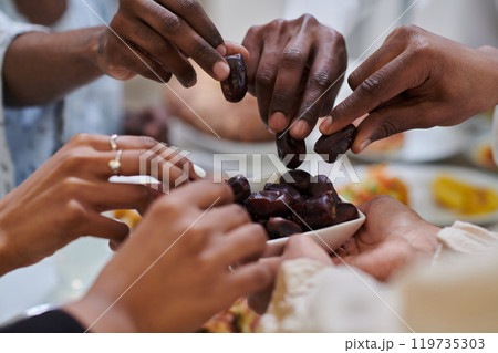 In a poignant close-up, the diverse hands of a Muslim family delicately grasp fresh dates, symbolizing the breaking of the fast during the holy month of Ramadan, capturing a moment of cultural unity 119735303