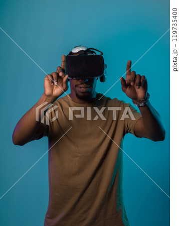 Immersed in a digital realm, an African American man navigates the virtual landscape with a VR goggles, using tactile gestures to interact with virtual objects, showcasing a harmonious blend of 119735400