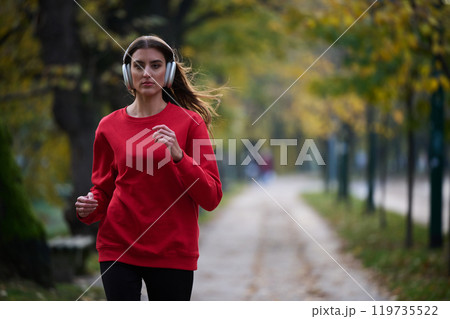 Young beautiful woman running in autumn park and listening to music with headphones on smartphone Young beautiful woman running in autumn park and listening to music with headphones on smartphone 119735522
