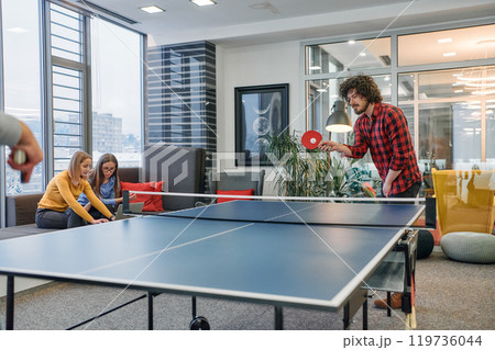 Business colleagues take a break from work to enjoy a game of table tennis, fostering teamwork and camaraderie in the workplace 119736044