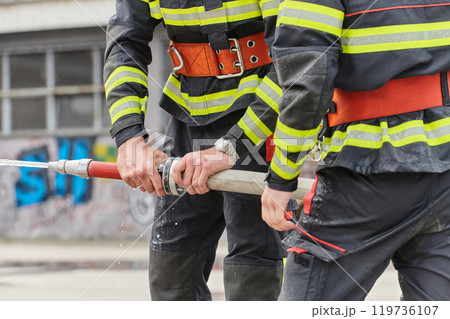 In a dynamic display of synchronized teamwork, firefighters hustle to carry, connect, and deploy firefighting hoses with precision, showcasing their intensive training and readiness for challenging 119736107