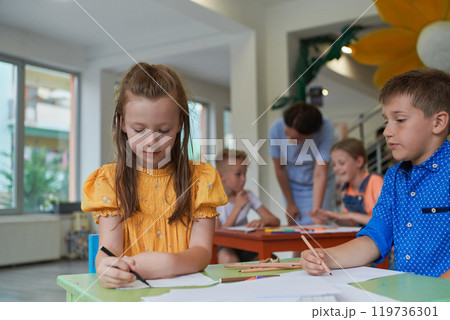 Creative kids during an art class in a daycare center or elementary school classroom drawing with female teacher. 119736301