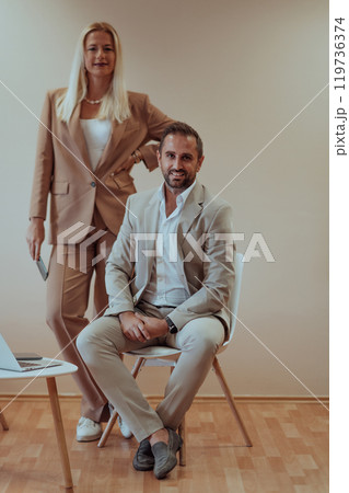 A business couple posing for a photograph together against a beige backdrop, capturing their professional partnership and creating a timeless image of unity and success. A business couple posing for a photograph together against a beige backdrop, capturing their professional partnership and creating a timeless image of unity and success. 119736374