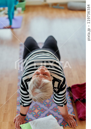 Senior Woman Practicing Back Stretches in a Sunlit Space for Optimal Health and Well Being Senior Woman Practicing Back Stretches in a Sunlit Space for Optimal Health and Well Being 119736384
