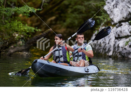 A young couple enjoying an idyllic kayak ride in the middle of a beautiful river surrounded by forest greenery 119736428