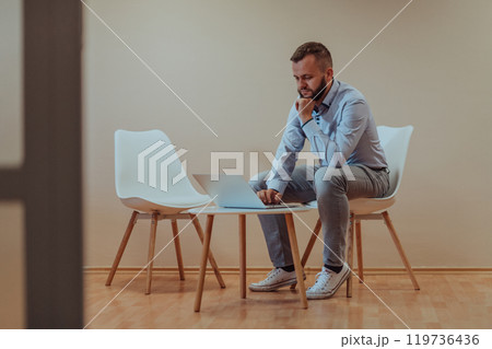 A confident businessman sitting and using laptop with a determined expression, while a beige background enhances the professional atmosphere, showcasing his productivity and expertise. 119736436