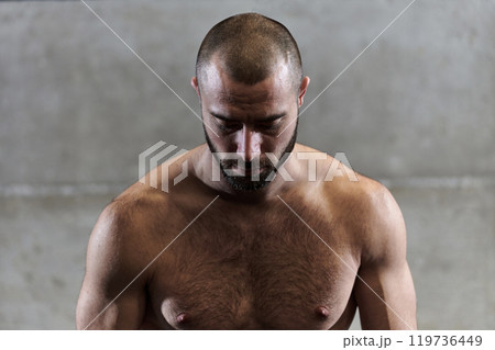 A muscular man poses in the gym, showcasing his strength and dedication to fitness through an impressive physique and glistening sweat on his face. 119736449