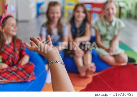 A happy female teacher sitting and playing hand games with a group of little schoolchildren A happy female teacher sitting and playing hand games with a group of little schoolchildren 119736455