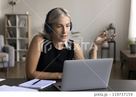 Aged female wearing headset speak on video conference by laptop 119737159